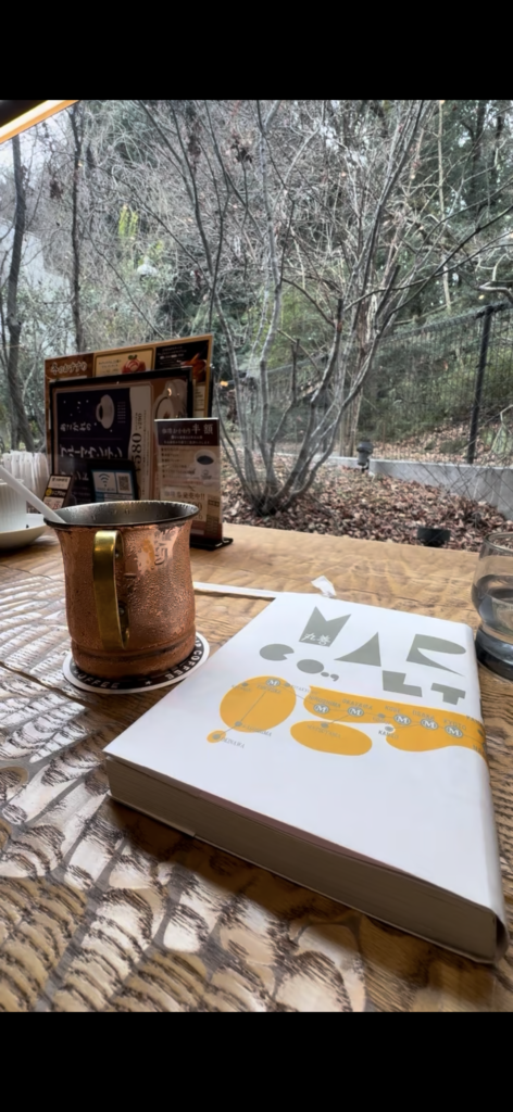 カフェの窓際で本を開き、飲み物とともに読書している様子